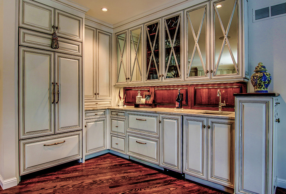 Photo of a large traditional l-shaped wet bar in St Louis with a submerged sink, recessed-panel cabinets, white cabinets, granite worktops, brown splashback and dark hardwood flooring.
