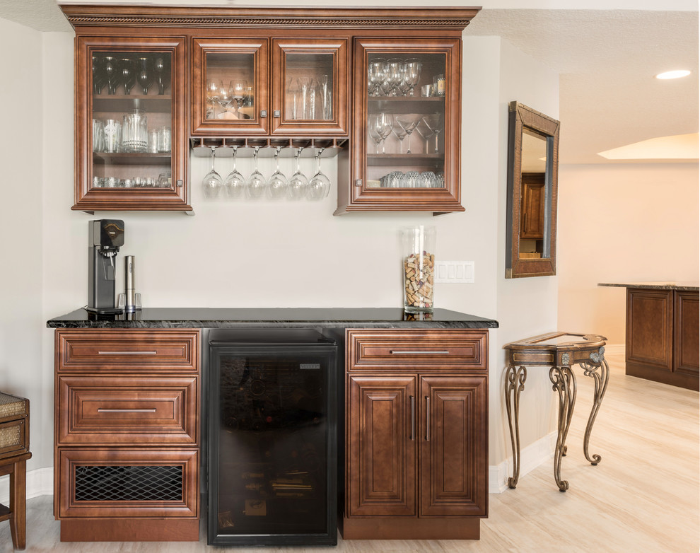 Inspiration for a mid-sized timeless single-wall vinyl floor and beige floor wet bar remodel in Orlando with no sink, raised-panel cabinets, medium tone wood cabinets, granite countertops and black countertops