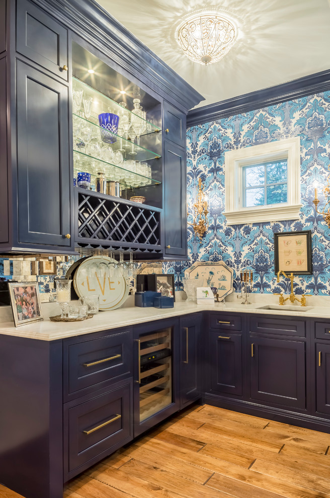 Inspiration för en mellanstor eklektisk l-formad hemmabar med vask, med en undermonterad diskho, luckor med profilerade fronter, blå skåp, marmorbänkskiva, spegel som stänkskydd och mellanmörkt trägolv