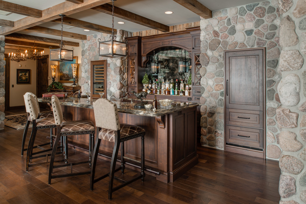 Immagine di un grande bancone bar classico con ante con bugna sagomata, ante in legno bruno, top in granito e pavimento in legno massello medio