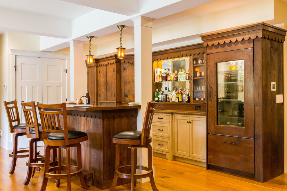 Diseño de bar en casa con barra de bar lineal clásico con armarios con paneles empotrados, puertas de armario de madera en tonos medios y suelo de madera en tonos medios