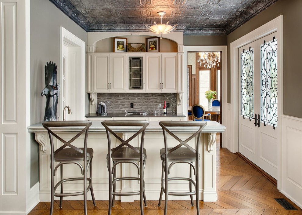 Klassische Hausbar mit Bartresen, profilierten Schrankfronten, weißen Schränken und Küchenrückwand in Grau in Sonstige