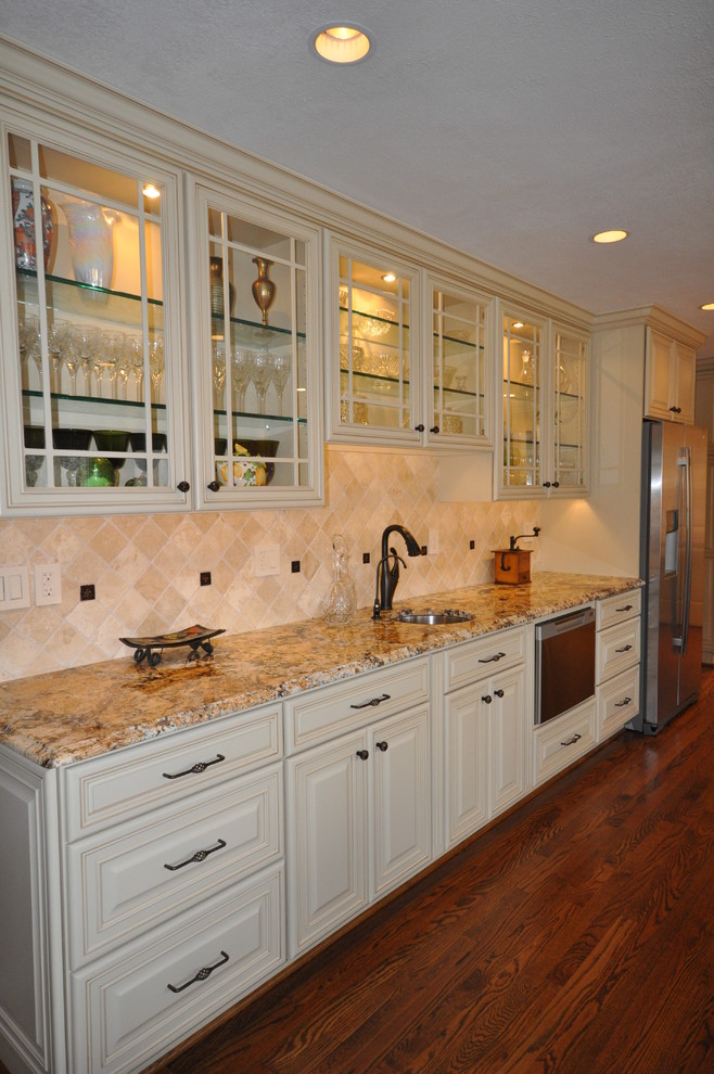 This is an example of a large traditional single-wall wet bar in DC Metro with a submerged sink, raised-panel cabinets, beige cabinets, beige splashback, dark hardwood flooring and brown floors.