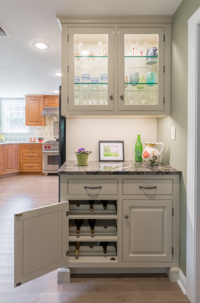 This is an example of a small classic single-wall wet bar in Philadelphia with no sink, glass-front cabinets, white cabinets, granite worktops, light hardwood flooring and beige floors.