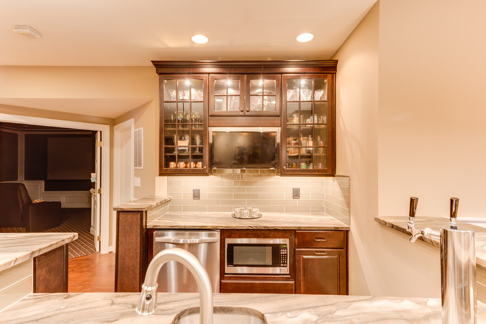 This is an example of a medium sized classic u-shaped wet bar in DC Metro with raised-panel cabinets, granite worktops, glass tiled splashback and medium hardwood flooring.