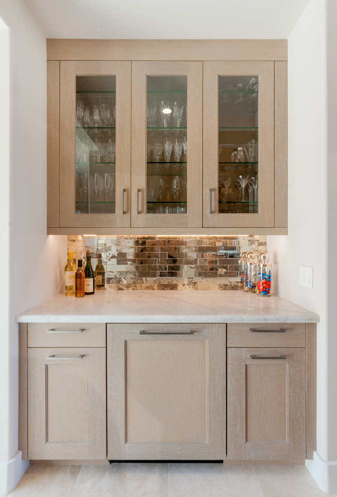 Cette photo montre un petit bar de salon linéaire chic en bois clair avec un plan de travail en granite, une crédence miroir, un sol en carrelage de céramique, un sol beige et un placard avec porte à panneau encastré.