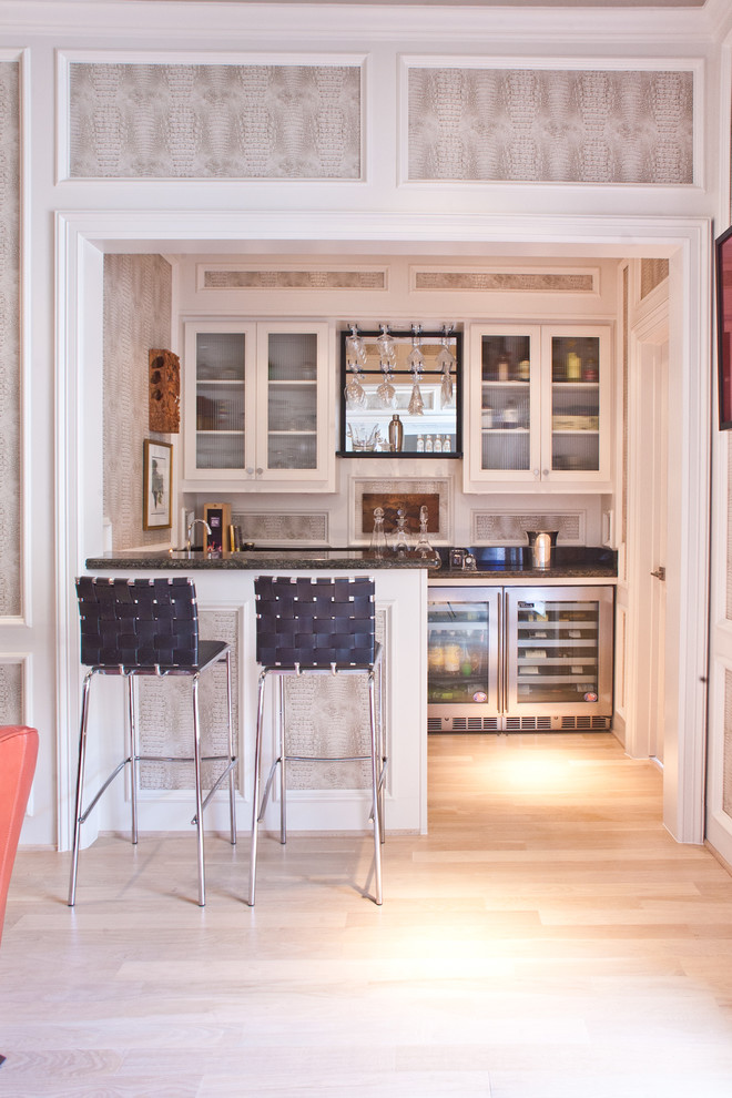 Cette photo montre un bar de salon chic en U avec des tabourets, un placard à porte vitrée, des portes de placard blanches et parquet clair.