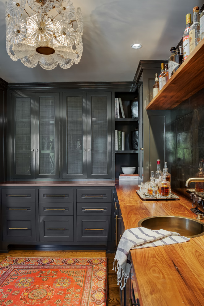Inspiration for a traditional l-shaped home bar in Portland with a built-in sink, recessed-panel cabinets, grey cabinets, wood worktops, black splashback, medium hardwood flooring, brown floors and brown worktops.