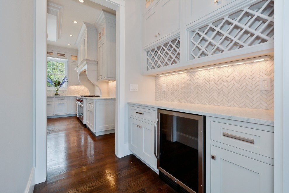 Wet bar - mid-sized traditional single-wall medium tone wood floor wet bar idea in New York with recessed-panel cabinets, white cabinets, marble countertops, white backsplash and ceramic backsplash