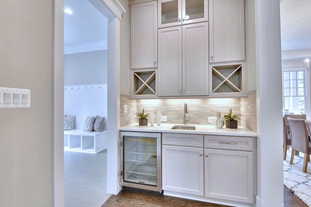 Photo of a medium sized traditional single-wall wet bar in DC Metro with a submerged sink, recessed-panel cabinets, beige cabinets, engineered stone countertops, beige splashback, matchstick tiled splashback, medium hardwood flooring and brown floors.