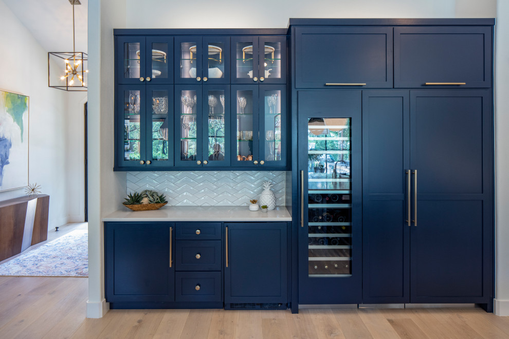 This is an example of a medium sized classic single-wall home bar in Austin with no sink, recessed-panel cabinets, blue cabinets, quartz worktops, white splashback, ceramic splashback, light hardwood flooring, beige floors and white worktops.