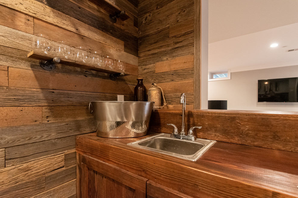 Inspiration for a large rustic l-shaped wet bar in Philadelphia with a built-in sink, distressed cabinets, wood worktops, brown splashback, tonge and groove splashback, grey floors and brown worktops.