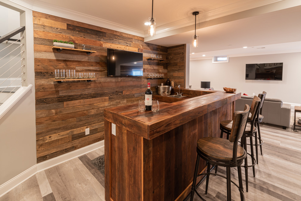 Photo of a large rustic l-shaped wet bar in Philadelphia with a built-in sink, distressed cabinets, wood worktops, brown splashback, tonge and groove splashback, grey floors and brown worktops.