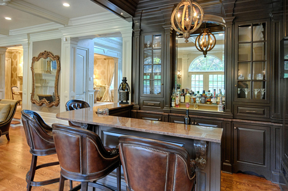 Diseño de bar en casa con barra de bar tradicional con armarios tipo vitrina, puertas de armario de madera en tonos medios y salpicadero con efecto espejo
