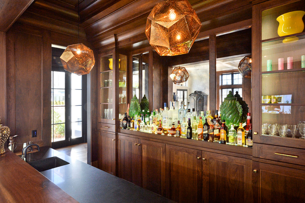 Cette image montre un bar de salon avec évier parallèle traditionnel en bois brun de taille moyenne avec un évier intégré, un placard à porte shaker, un plan de travail en bois, une crédence miroir et un sol en bois brun.