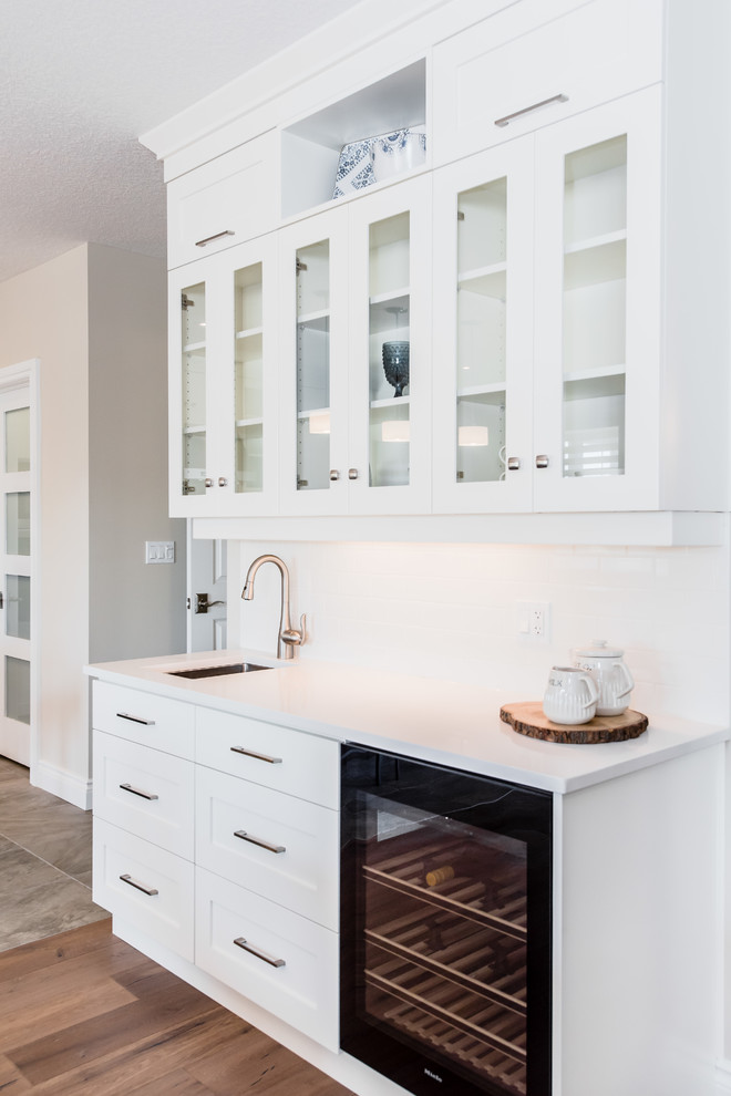 Inspiration for a small craftsman single-wall light wood floor wet bar remodel in Toronto with an undermount sink, glass-front cabinets, white cabinets, solid surface countertops, white backsplash and subway tile backsplash