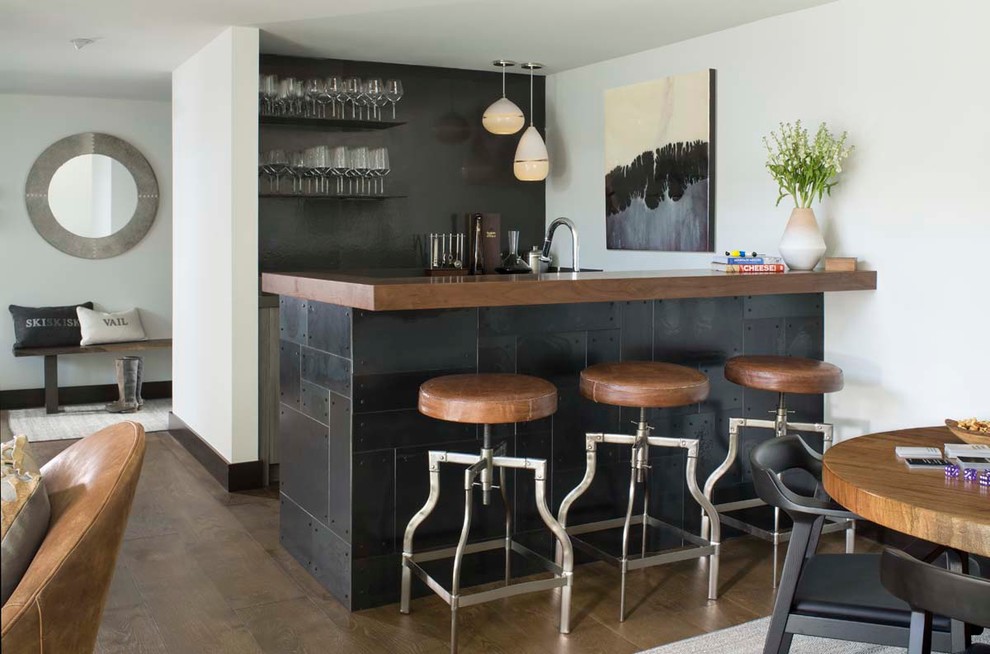 Стильный дизайн: п-образный домашний бар в современном стиле с барной стойкой, деревянной столешницей, черным фартуком и темным паркетным полом - последний тренд