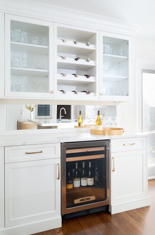 Home bar - transitional single-wall medium tone wood floor home bar idea in Philadelphia with shaker cabinets, white cabinets, quartz countertops, no sink, mirror backsplash and white countertops