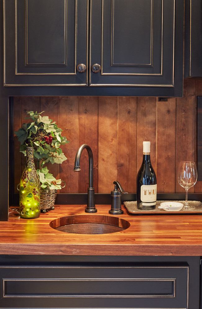 Foto på en liten medelhavsstil bruna linjär hemmabar med vask, med en undermonterad diskho, luckor med upphöjd panel, svarta skåp, träbänkskiva, brunt stänkskydd och ljust trägolv
