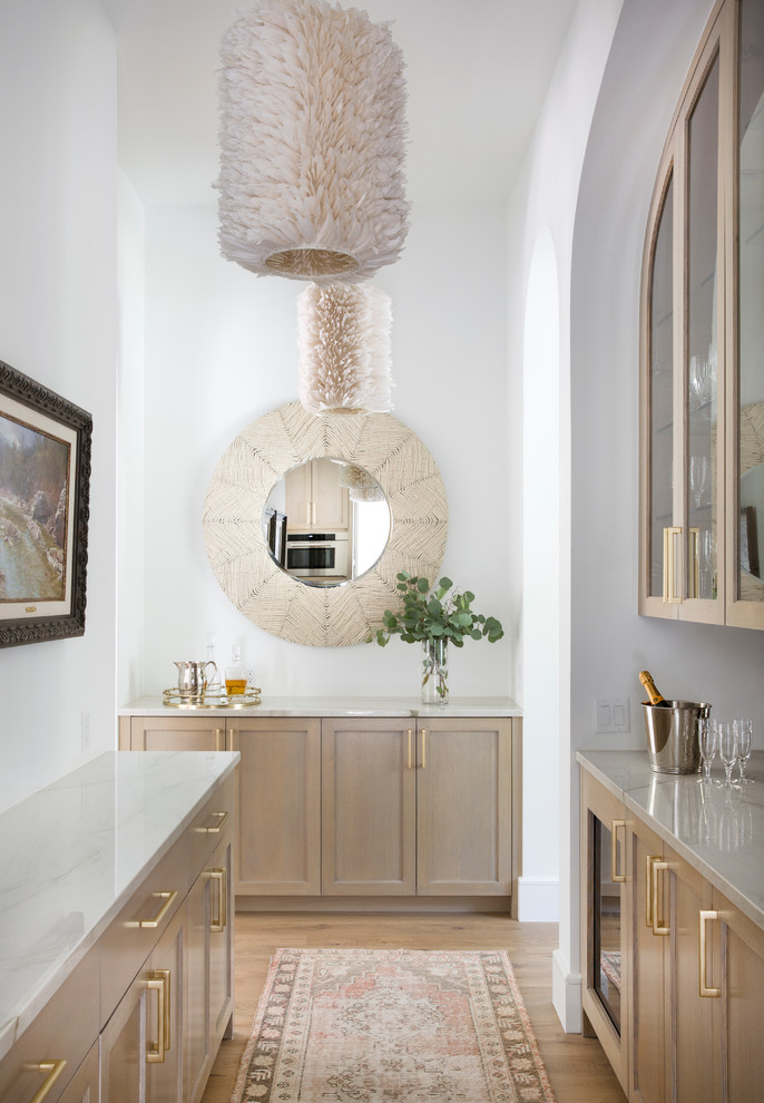 Zweizeilige Mediterrane Hausbar ohne Waschbecken mit Glasfronten, hellen Holzschränken, hellem Holzboden und weißer Arbeitsplatte in Austin