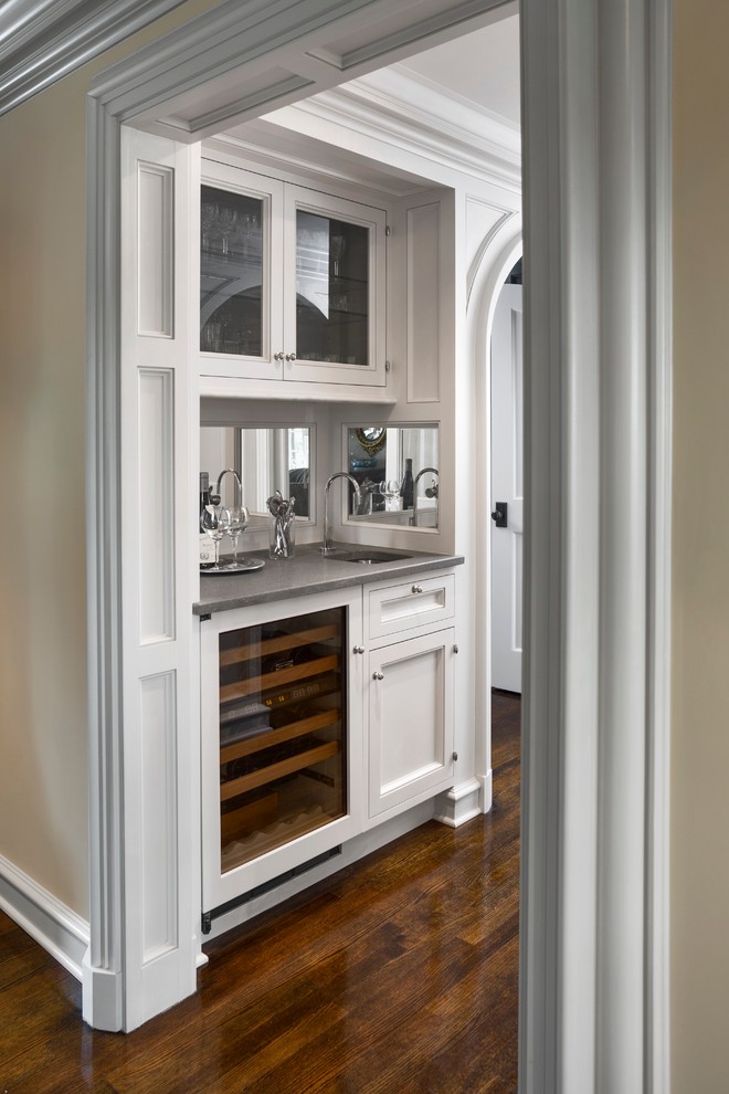 Foto på en mellanstor vintage grå linjär hemmabar med vask, med en undermonterad diskho, luckor med glaspanel, vita skåp, bänkskiva i koppar, spegel som stänkskydd, mörkt trägolv och brunt golv