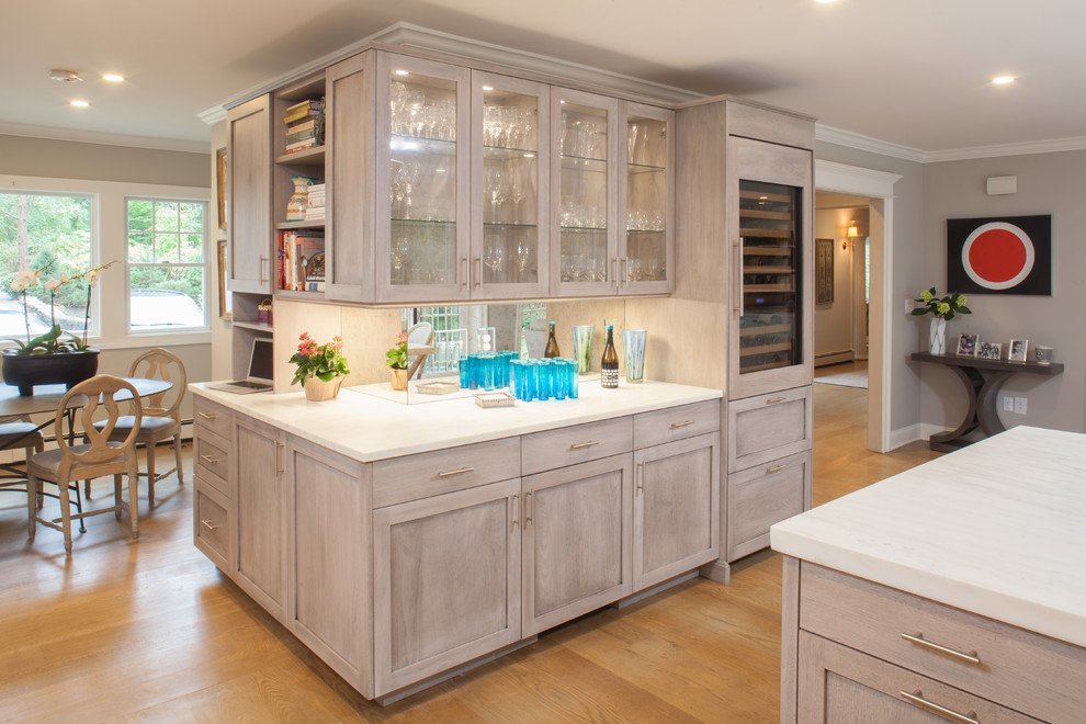 Inspiration for a large traditional l-shaped home bar in New York with recessed-panel cabinets, light wood cabinets, marble worktops and mirror splashback.