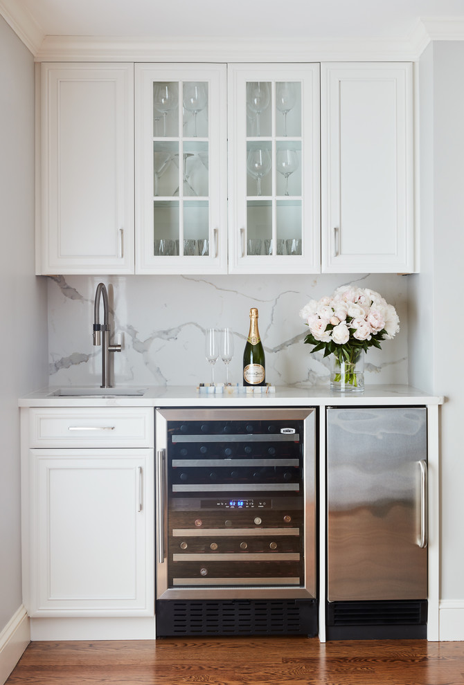 This is an example of a small contemporary single-wall wet bar in Boston with glass-front cabinets, white cabinets, quartz worktops, white splashback, dark hardwood flooring and brown floors.