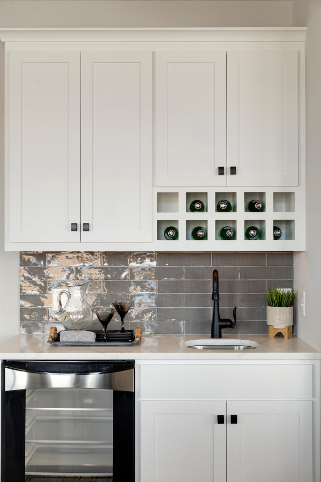 Transitional single-wall medium tone wood floor wet bar photo in Minneapolis with an undermount sink, shaker cabinets, white cabinets, quartzite countertops, gray backsplash, subway tile backsplash and white countertops