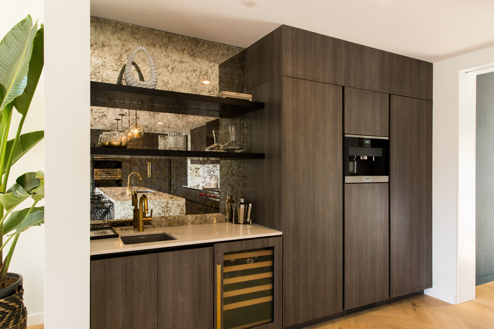 Example of a large minimalist single-wall light wood floor wet bar design in Los Angeles with an undermount sink, flat-panel cabinets, dark wood cabinets, marble countertops, glass sheet backsplash and white countertops