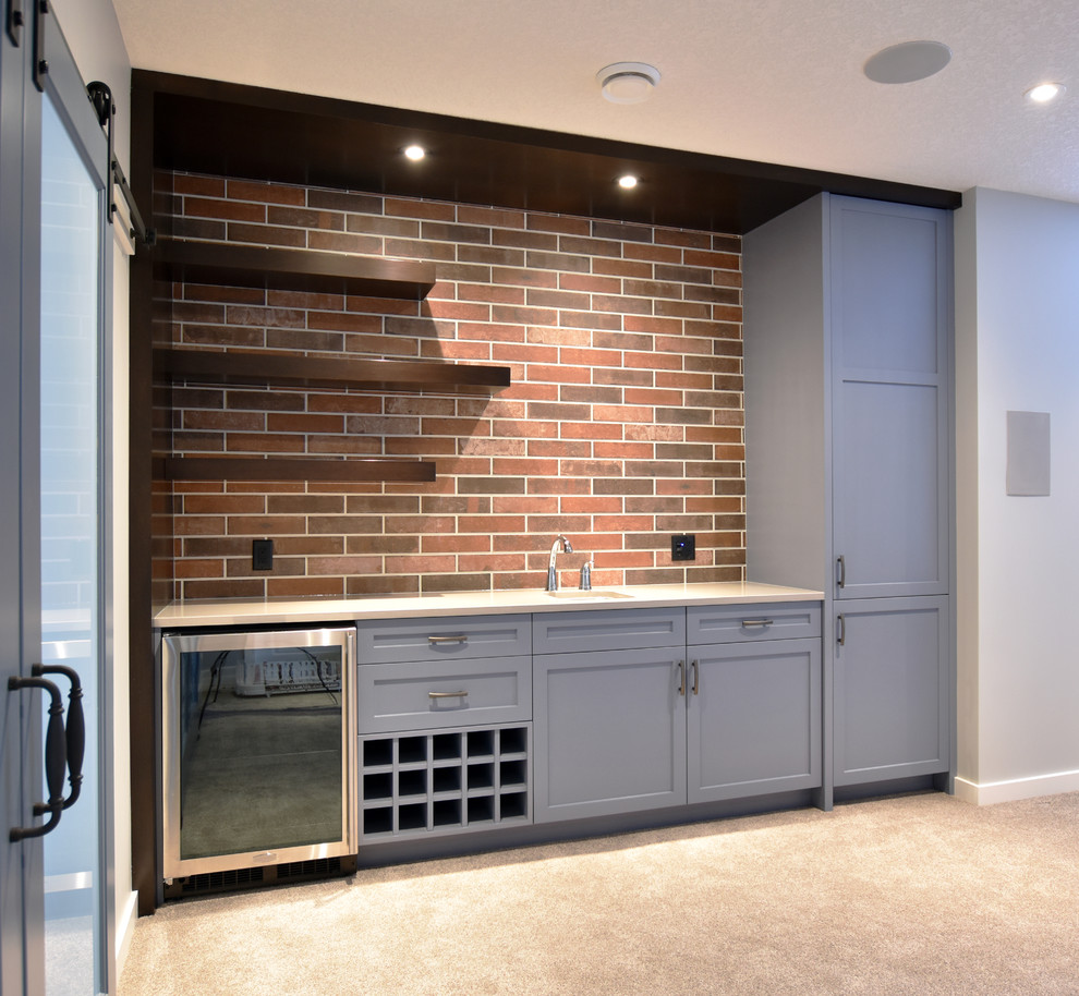 This is an example of a medium sized contemporary single-wall wet bar in Calgary with a submerged sink, shaker cabinets, blue cabinets, engineered stone countertops, carpet and beige floors.