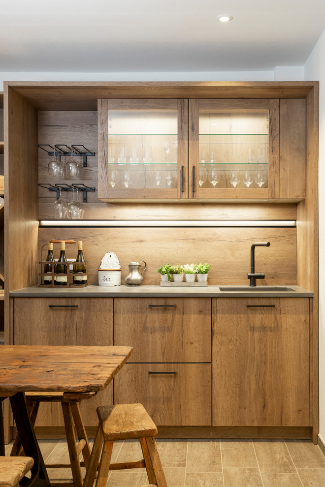 Cette photo montre un bar de salon avec évier linéaire tendance en bois clair avec un placard à porte vitrée, une crédence en bois, un sol beige et un plan de travail gris.