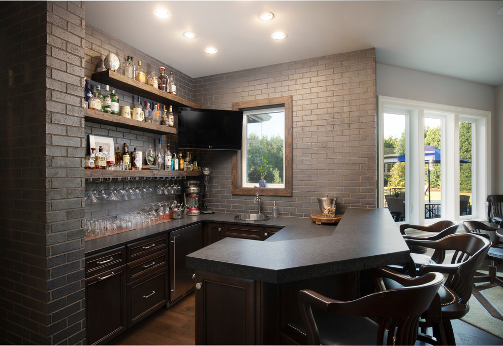 Seated home bar - mid-sized transitional galley medium tone wood floor and brown floor seated home bar idea in Portland with a drop-in sink, recessed-panel cabinets, dark wood cabinets, granite countertops, gray backsplash, brick backsplash and black countertops