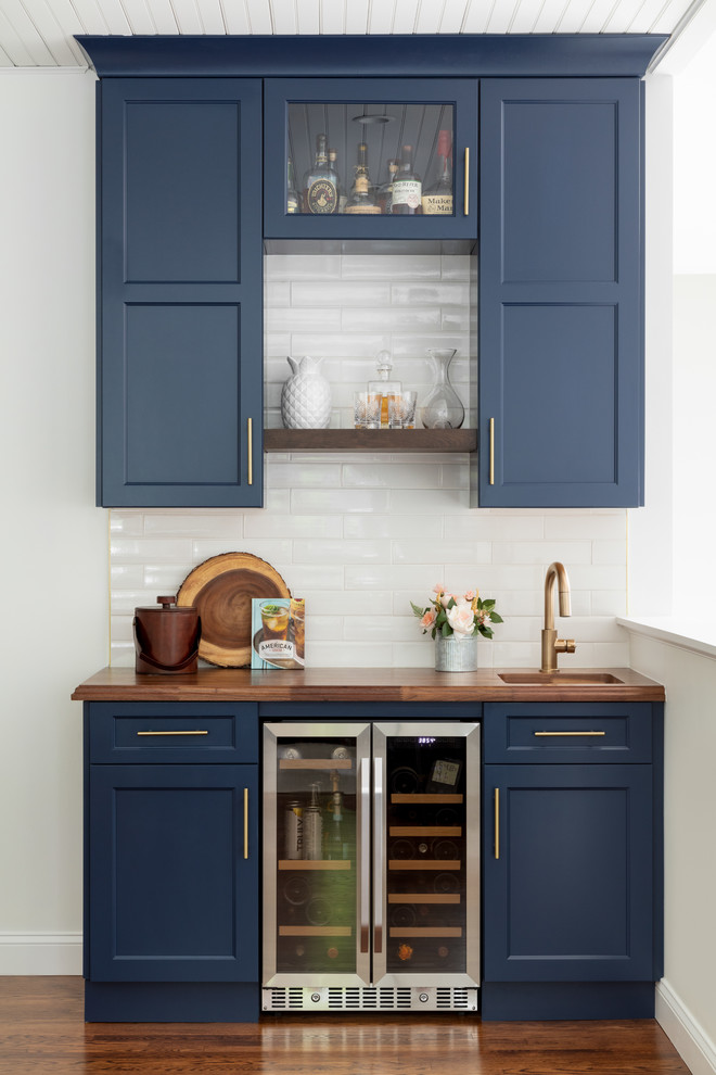 Wet bar - small country single-wall medium tone wood floor and brown floor wet bar idea in Boston with an undermount sink, shaker cabinets, blue cabinets, wood countertops, white backsplash, subway tile backsplash and brown countertops