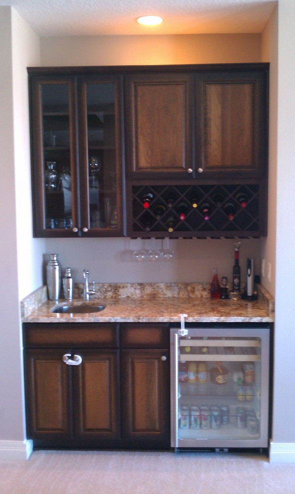 Wet bar - small traditional single-wall porcelain tile wet bar idea in Tampa with an undermount sink, raised-panel cabinets, dark wood cabinets and granite countertops