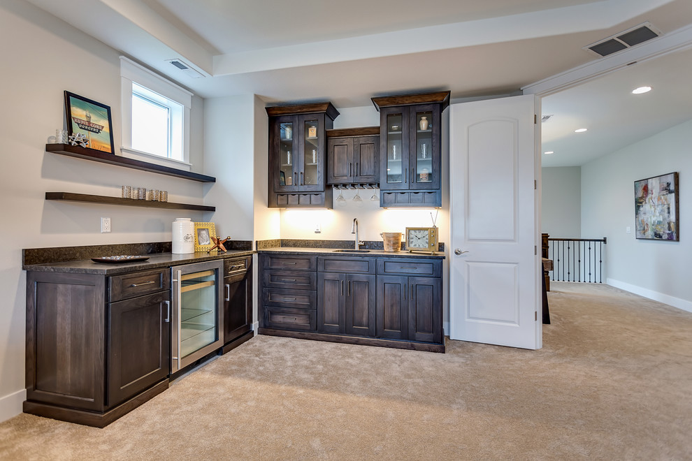 Expansive traditional l-shaped wet bar in Portland with carpet, a submerged sink, recessed-panel cabinets, dark wood cabinets, granite worktops, multi-coloured splashback and stone slab splashback.
