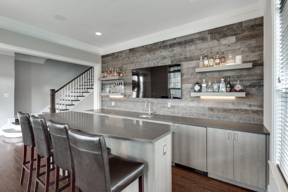 Large classic wet bar in DC Metro with a submerged sink, flat-panel cabinets, grey cabinets, grey splashback, wood splashback, medium hardwood flooring, brown floors and a feature wall.
