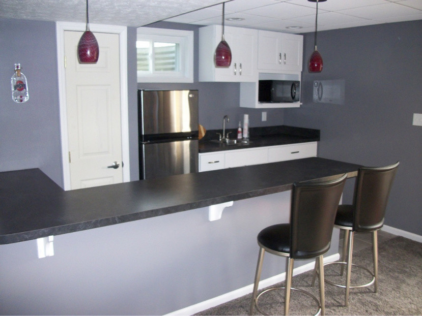 Photo of a modern l-shaped home bar in Cincinnati with a built-in sink, white cabinets, laminate countertops and ceramic flooring.