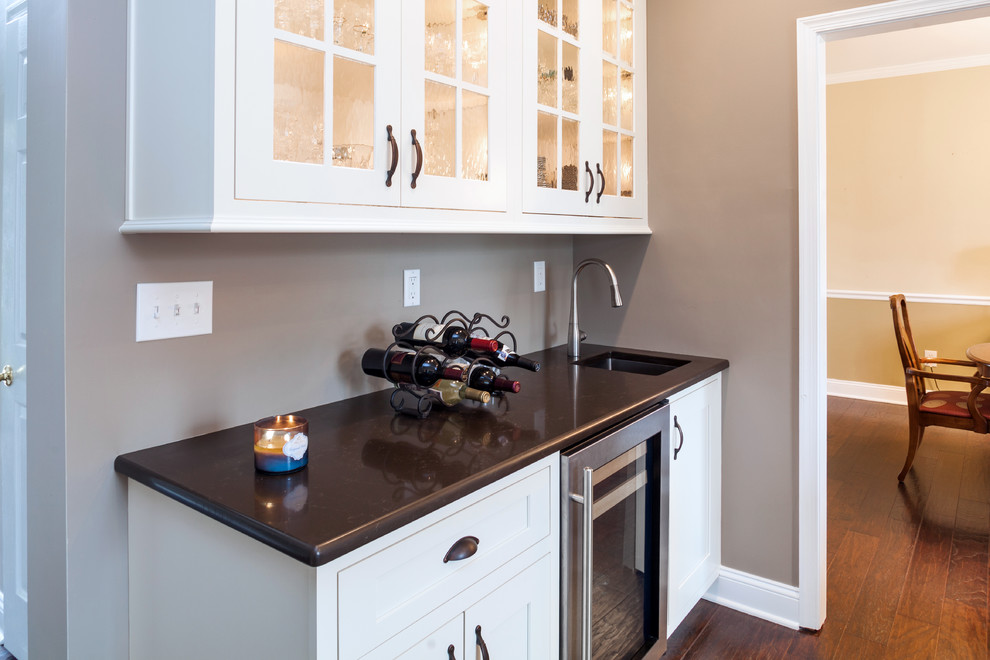 Medium sized traditional single-wall wet bar in Philadelphia with dark hardwood flooring, a submerged sink, glass-front cabinets, white cabinets, marble worktops, brown floors and brown worktops.