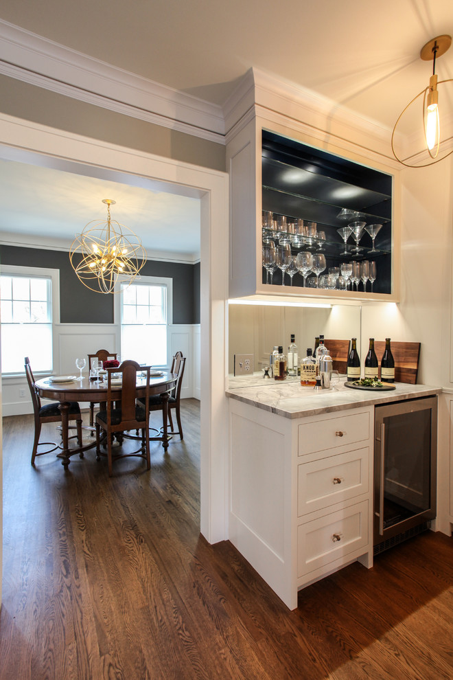 Inspiration for a small contemporary single-wall home bar in Minneapolis with no sink, white cabinets, marble worktops, mirror splashback, medium hardwood flooring, shaker cabinets, brown floors and grey worktops.