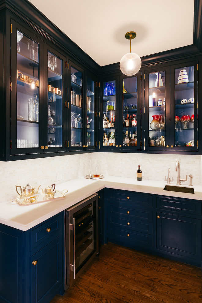 Foto på en mellanstor vintage l-formad hemmabar med vask, med en undermonterad diskho, luckor med glaspanel, blå skåp, marmorbänkskiva, vitt stänkskydd, stänkskydd i porslinskakel och mörkt trägolv