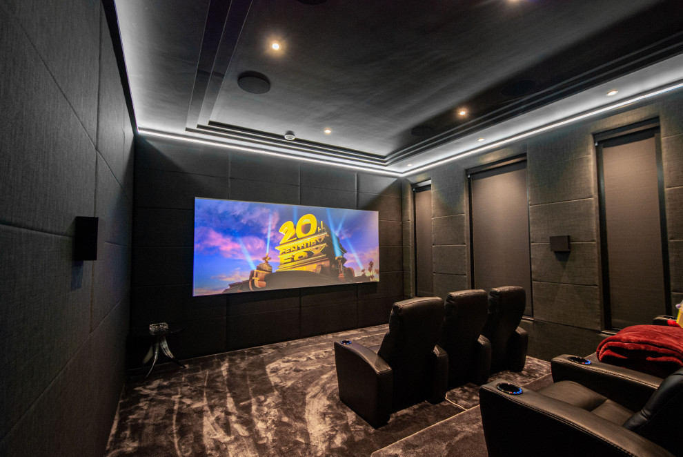 Photo of a large modern enclosed home cinema in Surrey with black walls, carpet, a projector screen and grey floors.