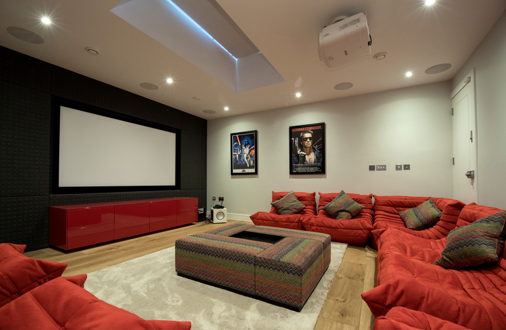 Photo of a large traditional enclosed home cinema in London with grey walls, light hardwood flooring and a projector screen.