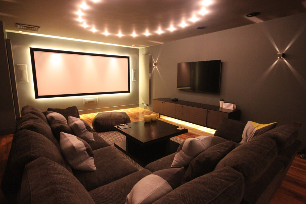 Photo of a medium sized contemporary enclosed home cinema in London with grey walls, medium hardwood flooring and a projector screen.