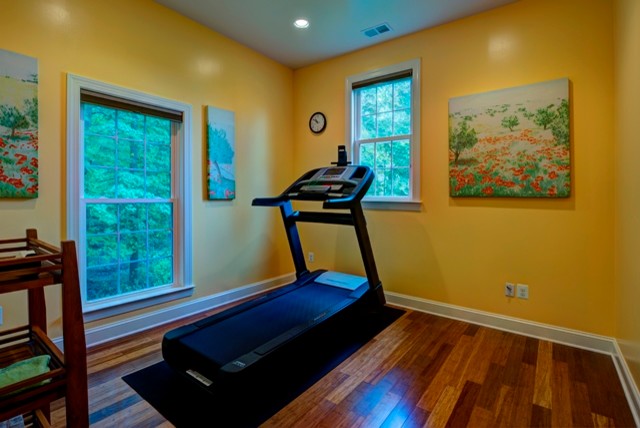 Aménagement d'une petite salle de sport classique multi-usage avec un mur jaune et un sol en bois brun.