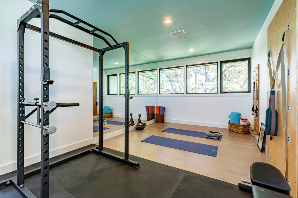 Multifunktionaler, Großer Moderner Fitnessraum mit weißer Wandfarbe, hellem Holzboden und braunem Boden in Austin