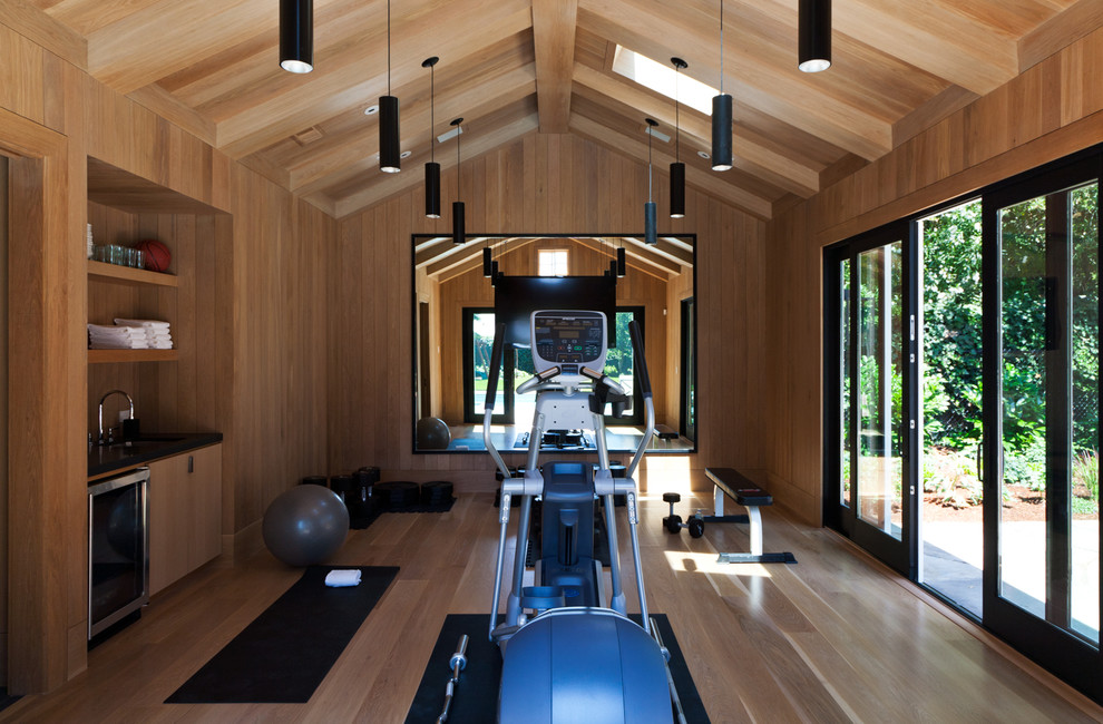 Imagen de sala de pesas contemporánea extra grande con paredes marrones, suelo de madera clara y suelo marrón