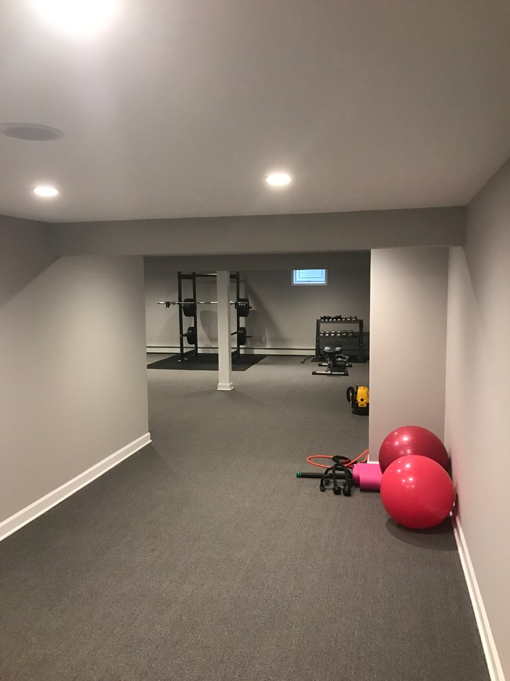 Imagen de sala de pesas clásica grande con paredes grises, moqueta y suelo gris