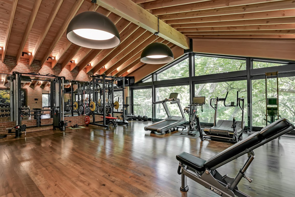 Foto de sala de pesas de estilo americano extra grande con paredes rojas, suelo de madera oscura y suelo marrón