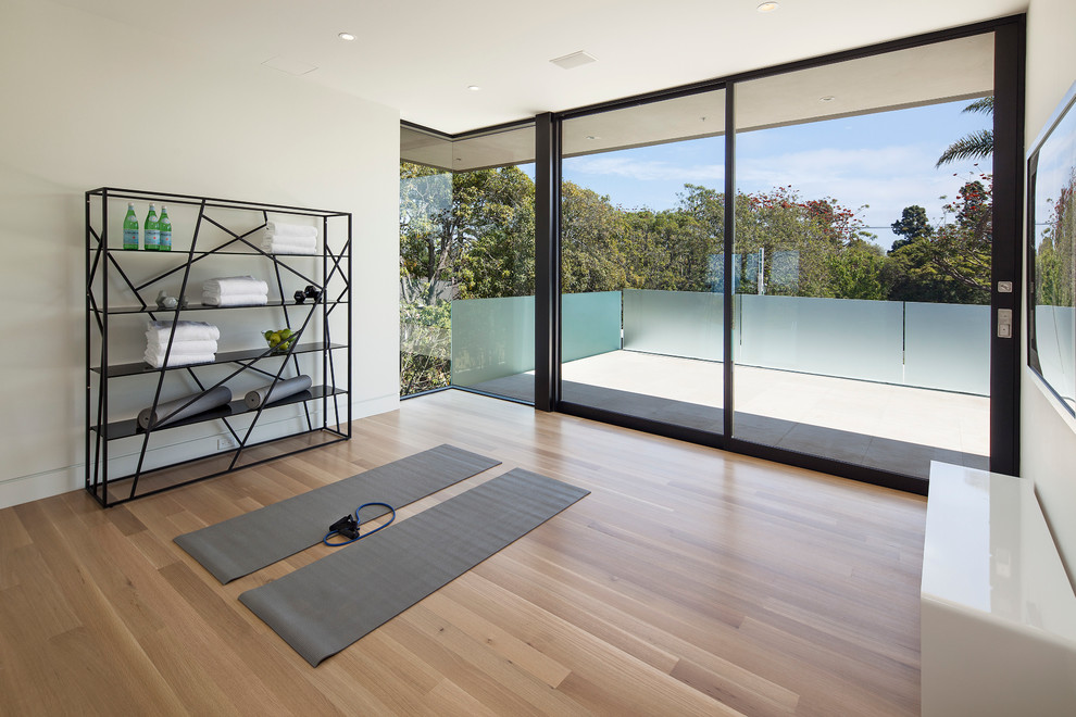 Imagen de estudio de yoga contemporáneo de tamaño medio con paredes blancas, suelo de madera clara y suelo marrón