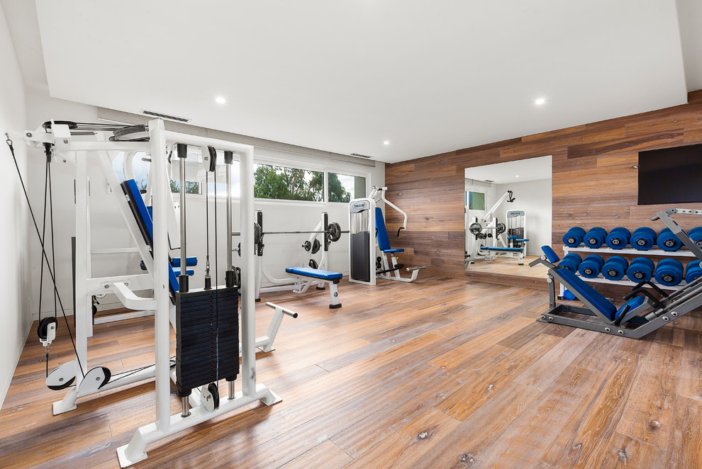Multifunktionaler Moderner Fitnessraum mit weißer Wandfarbe und dunklem Holzboden in Melbourne